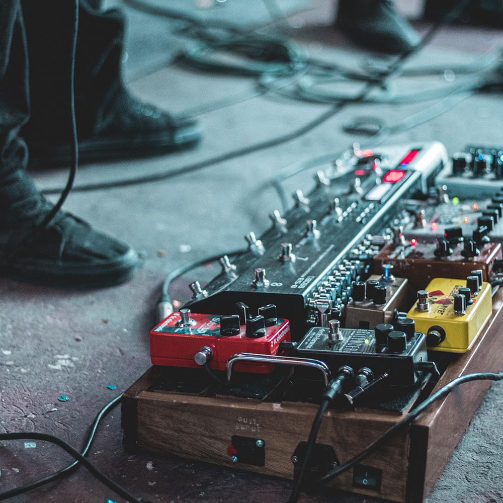 Cover art of “I've Been Running Through the Static” by Wolferfoxxx: a guitar pedalboard with red and yellow pedals and a player's black sneakers on a concrete stage floor.